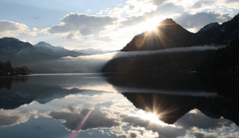 Der Grundlsee mit einer wunderschönen spiegelung der Sonne hinter einem Berg.